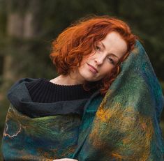 a woman with red hair wrapped in a green and yellow blanket looking at the camera