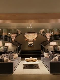 a living room filled with lots of furniture next to a stair case and chandelier