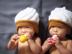 two babies wearing knitted hats and holding food in their mouths while standing next to each other