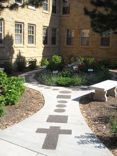 a walkway leading to a building with flowers in the foreground and a bench on the other side