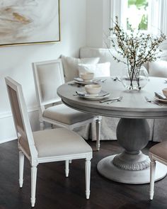 a dining room table with chairs and a vase on top of it in front of a window