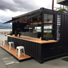 an outdoor bar with tables and stools next to the water on a cloudy day