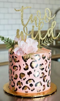 a pink leopard print cake with gold lettering and flowers on top, sitting on a table