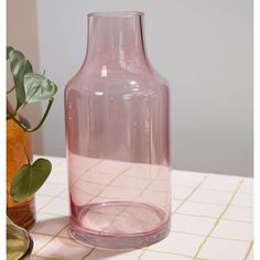 a pink vase sitting on top of a table next to a potted plant