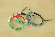 three bracelets are sitting on top of a wooden table, one is green and the other is red