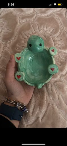 a hand holding a green turtle shaped bowl with hearts on it's sides and the lid