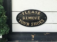 a sign that says please remove your shoes on the side of a wall next to potted plants