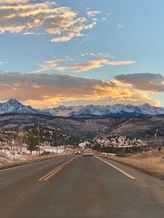 a car is driving down the road in front of some mountains and snow covered hills