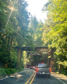 cars are driving down the road in front of an entrance to national park on a sunny day