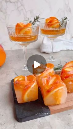 three glasses filled with orange slices on top of a wooden cutting board