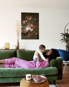 a woman laying on top of a green couch next to a little boy in pink pants