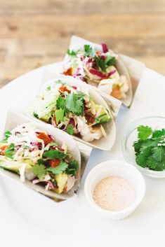 three tacos with different toppings sit on a plate next to a small bowl of dressing