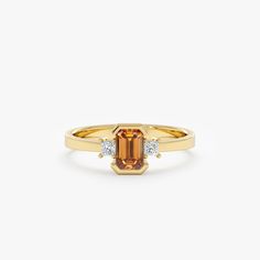 a yellow gold ring with an orange stone and two white diamonds on the side, set in