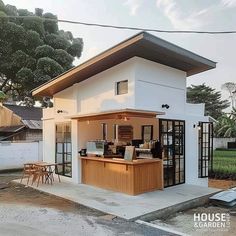 a small white house with an open kitchen and dining area on the front porch, next to a fenced in yard