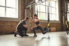 two people in a gym doing exercises on rings and pull ups with one person holding the other's leg