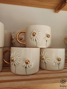 white ceramic cups with gold handles and daisies on the rims are sitting on a shelf