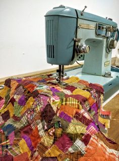 an old blue sewing machine sitting on top of a quilted tablecloth covered with multicolored fabric