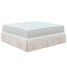 a white ottoman with fringe trim on it's sides and bottom part, in front of a white background