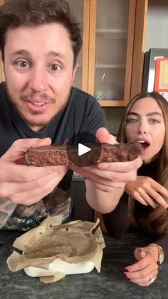 a man and woman are looking at a piece of chocolate cake on the counter top