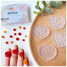 a person's hand next to some fake flowers and plastic hearts on a table