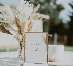 the table numbers are placed next to a vase with dry grass in it and a candle