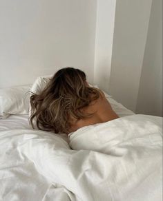 a woman laying in bed with white sheets