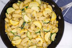 a skillet filled with pasta and zucchini on top of a white table