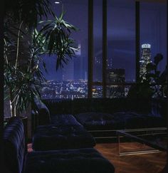 a living room filled with furniture and a large window overlooking the city at night time