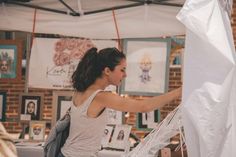 a woman is shopping at an outdoor market with her hand on the white fabric hanging from it