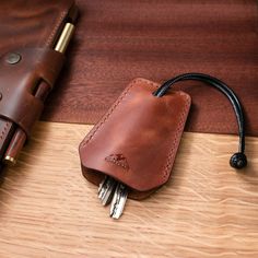 a leather case with keys in it sitting on a wooden table next to a pen