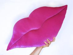 a pink pillow being held up by a person's hand on a white background