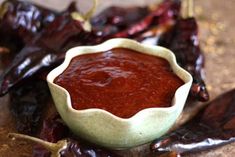 a bowl filled with red chili sauce sitting on top of a wooden table next to dried peppers