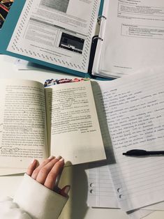 a person's hand resting on an open book next to several papers and pens