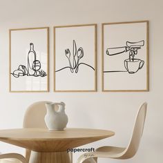 three black and white drawings hang on the wall next to a table with two chairs