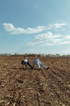 two men sitting in the middle of a plowed field, one is holding onto another man's leg