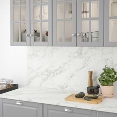 a kitchen with gray cabinets and white marble counter tops, along with a cutting board that has rocks on it