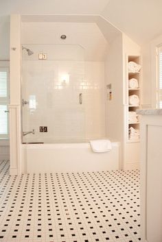 a white bathroom with black and white tile flooring on the shower wall, tub and shelves