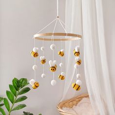 a white and yellow mobile with bees hanging from it's sides next to a potted plant