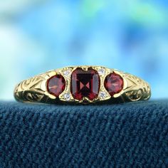 The ring features a vintage style, characterized by intricate carved detailing and a timeless aesthetic. The yellow gold setting offers a warm and rich backdrop for the gemstones. At the heart of the ring are three natural vibrant red garnets. Complementing the garnets are natural diamonds, round in shape and carefully placed to add sparkle and elegance. A perfect addition to any jewelry collection, this ring brings a touch of vintage charm to every special occasion. CHARACTERISTICS Status: Made to order Origin: Thailand Metal: Solid 9K Yellow Gold Ring Size: US 3-8 Total Gemstones Weight: 0.72 carat. (approx.) Total Gram Weight: 2.00 g. (approx.) *Pictures have been enlarged to show details* PRIMARY STONE(S) Stone: Natural Garnet Color: Red Shape: Oval Size: 4 x 3.5, 3 mm. Number: 3 Weigh Luxury Three Stone Ruby Ring For Wedding, Luxury Ruby Ring With Gemstone Accents For Anniversary, Luxury Ruby Three Stone Rings, Gold Heirloom Ruby Ring With Gemstone Accents, Luxury Red Three Stone Jewelry, Heirloom Gold Ruby Ring With Gemstone Accents, Yellow Gold Ruby Ring With Intricate Design For Promise, Luxury Red Three-stone Jewelry, Luxury Ruby Rings With Intricate Design