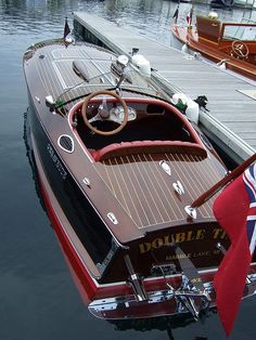 a small boat docked at a dock with other boats in the water and flags flying from it