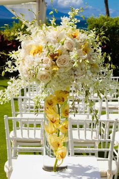 a vase filled with white and yellow flowers sitting on top of a table next to chairs