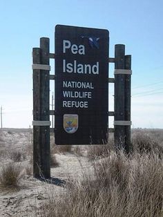 a sign for pea island national wildlife refuge in the middle of an open field with dry grass