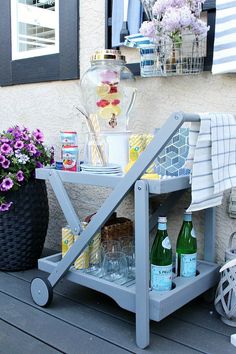 an outdoor table with drinks and flowers on the back porch area, next to a potted plant