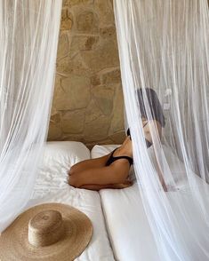 a woman laying on top of a bed covered in white netting next to a straw hat