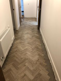 an empty hallway with wood flooring and white walls, leading to another room on the other side