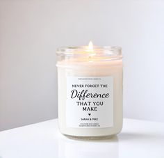 a white candle with a quote on it sitting on a table next to a cup