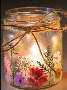 a glass jar with flowers painted on the inside and string wrapped around it's lid