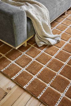 a couch with a blanket on top of it next to a rug and wooden floor