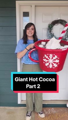 a woman holding a giant red bucket filled with cotton in front of a door that says giant hot cocoa part 2