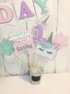 a cup filled with cake toppers sitting on top of a white table next to a sign that says happy birthday